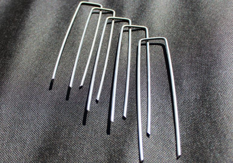 Silver metal U-stakes for securing landscape fabric or garden netting.