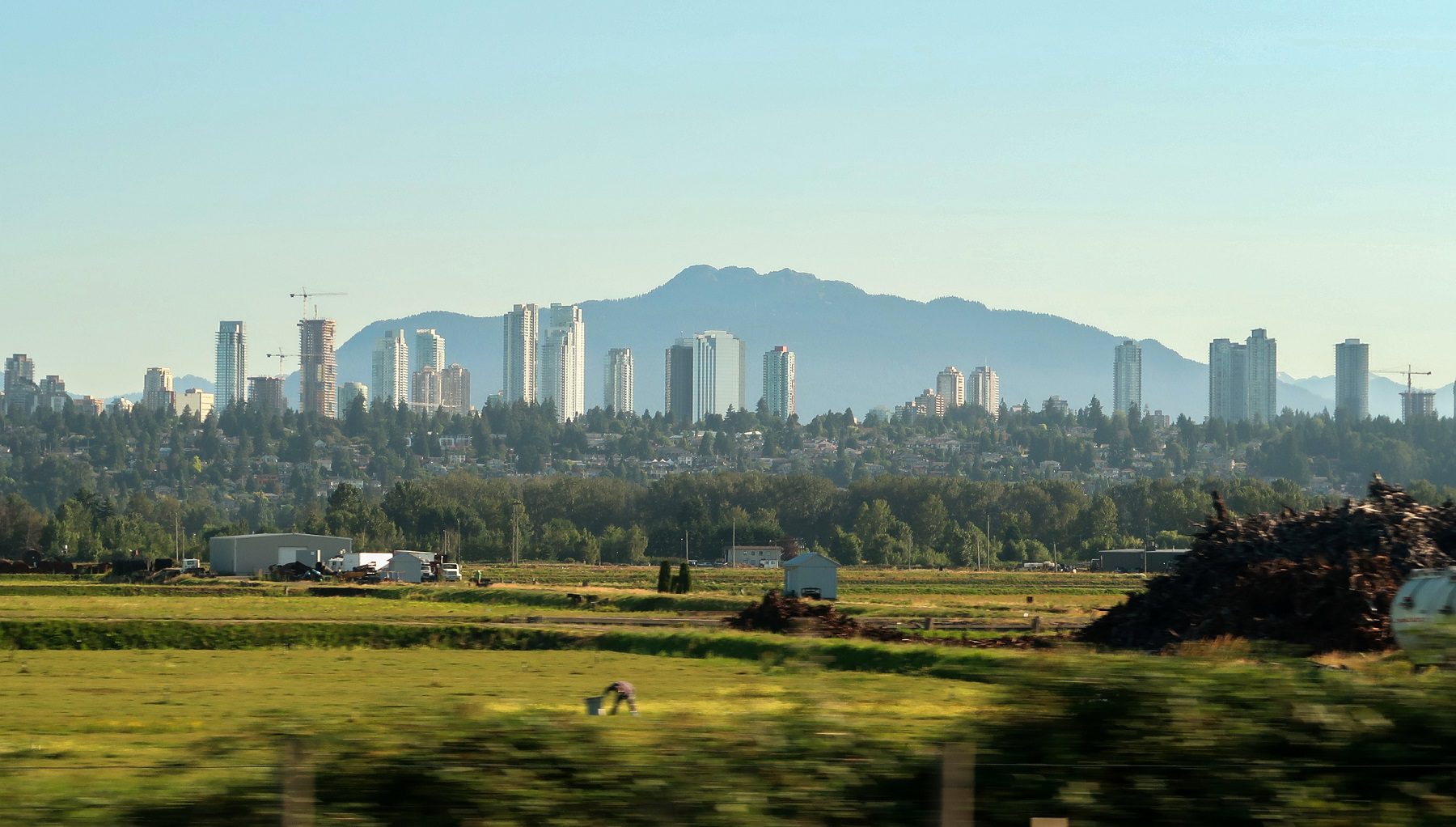 City skyscrapers backed by mountains, overlooking foreground farmland and forest.